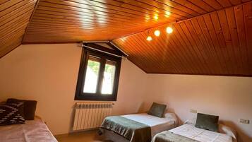Een gezellig slaapkamer op zolder met houten schuine plafonds, twee eenpersoonsbedden, een raam en een radiator.