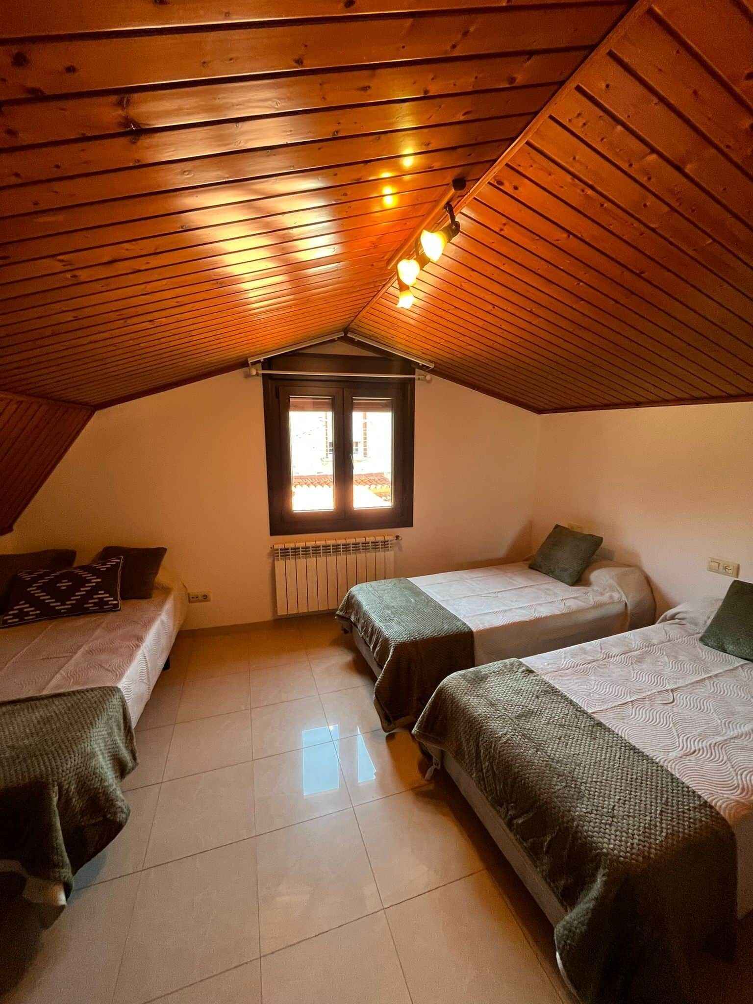 A dormitory room with two beds, a window, and a sloped ceiling.