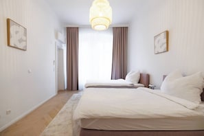 Ein Hotelzimmer mit zwei Betten, einem großen Fenster mit Vorhängen, einer Pendelleuchte und zwei gerahmten Bildern an den Wänden.