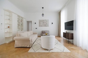 Ein modernes Wohnzimmer mit einer Couch, Hocker, Fernseher und Bücherregal.