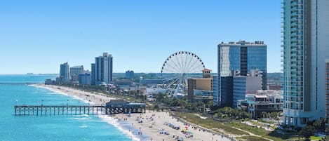 A coastal cityscape with a beach, a pier, and a large Ferris wheel.