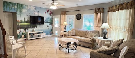 A living room with a television, sofa, chairs, a coffee table, and a decorative wall mural.