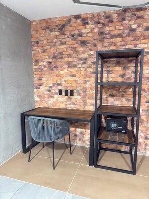 A corner room with a brick wall, a wooden desk, a chair, and a black metal shelving unit. - Hotel Van Gogh (El Salto)