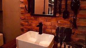 Ein Badezimmer mit einem weißen Waschbecken, einem Spiegel, einem Handtuchhalter und einer Ziegelwand.