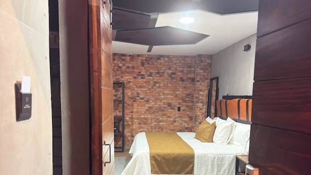 Ein Hotelzimmer mit Backsteinwand, einem Bett mit weißer Bettwäsche, einer Holztür und einem gefliesten Boden.