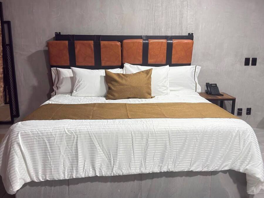 Quarto moderno com uma cama grande, cabeceira com painéis quadrados, telefone ao lado da cama e luminária fixada na parede.