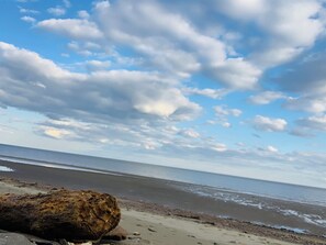 Ein Strand mit einem großen Felsen im Vordergrund und einem klaren Himmel mit Wolken.