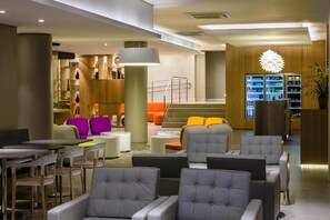 Eine moderne Lobby mit Sitzbereichen, einer Treppe und einem Getränkekühlschrank.