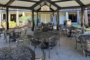 Ein überdachter Patio-Bereich mit mehreren Tischen und Stühlen, einem Schild mit der Aufschrift 'Sidewalk Cafe' und einem Gebäudeeingang im Hintergrund.