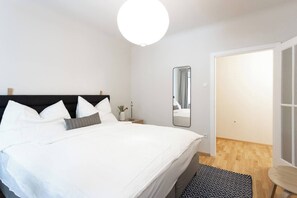Ein Schlafzimmer mit Bett, Nachttisch, Spiegel und einer Tür zu einem anderen Raum.