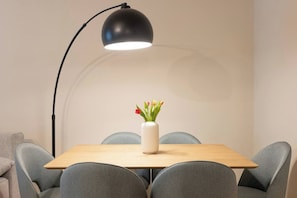 Una mesa de comedor con un jarrón de flores, rodeada de sillas, bajo una lámpara de pie.