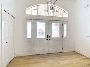 Ein Zimmer mit Holzboden, weißen Wänden und einem großen, rundbogenförmigen Fenster über einem Paar Doppeltüren mit Glasfeldern.