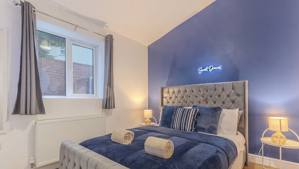 A bedroom with a tufted headboard, a large window with curtains, a neon sign, and two bedside lamps. - Crème Da La Casa (Coventry)