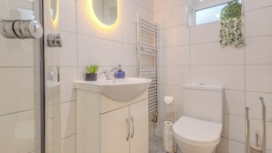 A modern bathroom with a white sink, mirror, and toilet, a towel rack, and a window with a plant. - Crème Da La Casa (Coventry)