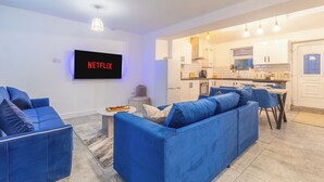A modern living room with a blue sofa, a flat-screen TV, and a kitchen in the background. - Crème Da La Casa (Coventry)