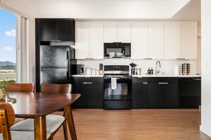 A modern kitchen with black appliances, white cabinets, and a dining area with a wooden table and chairs. - Stylish Art District Retreat | Walk to little Tokyo (Los Angeles)