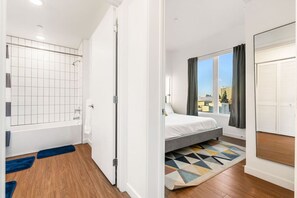 A modern bedroom with a shower, a bed, a view of buildings, and a window with curtains. - Stylish Art District Retreat | Walk to little Tokyo (Los Angeles)
