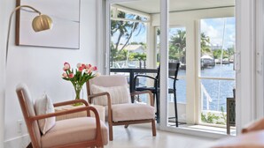 A modern living room with a view of a marina, featuring two wooden chairs, a small table, and a vase with flowers. - Waterfront 3 King Suites - Dock + Pool Near Beach - Paddleboards Included (Fort Lauderdale)