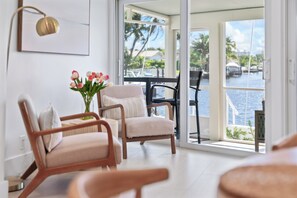 A modern living room with a view of a marina, featuring two wooden chairs, a small table, and a vase with flowers. - Waterfront 3 King Suites - Dock + Pool Near Beach - Paddleboards Included (Fort Lauderdale)