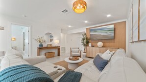 A modern living room with a white sofa, a coffee table, and a wooden cabinet. - Waterfront 3 King Suites - Dock + Pool Near Beach - Paddleboards Included (Fort Lauderdale)