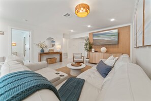 A modern living room with a white sofa, a coffee table, and a wooden cabinet. - Waterfront 3 King Suites - Dock + Pool Near Beach - Paddleboards Included (Fort Lauderdale)