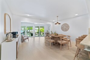 A modern kitchen with a dining area, wooden chairs, a round table, and a view of the outdoors. - Waterfront 3 King Suites - Dock + Pool Near Beach - Paddleboards Included (Fort Lauderdale)