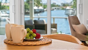 A table with two white mugs, a plate of fruit, and a view of a marina through large windows. - Waterfront 3 King Suites - Dock + Pool Near Beach - Paddleboards Included (Fort Lauderdale)