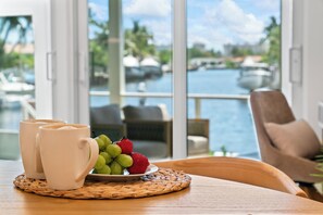 A table with two white mugs, a plate of fruit, and a view of a marina through large windows. - Waterfront 3 King Suites - Dock + Pool Near Beach - Paddleboards Included (Fort Lauderdale)