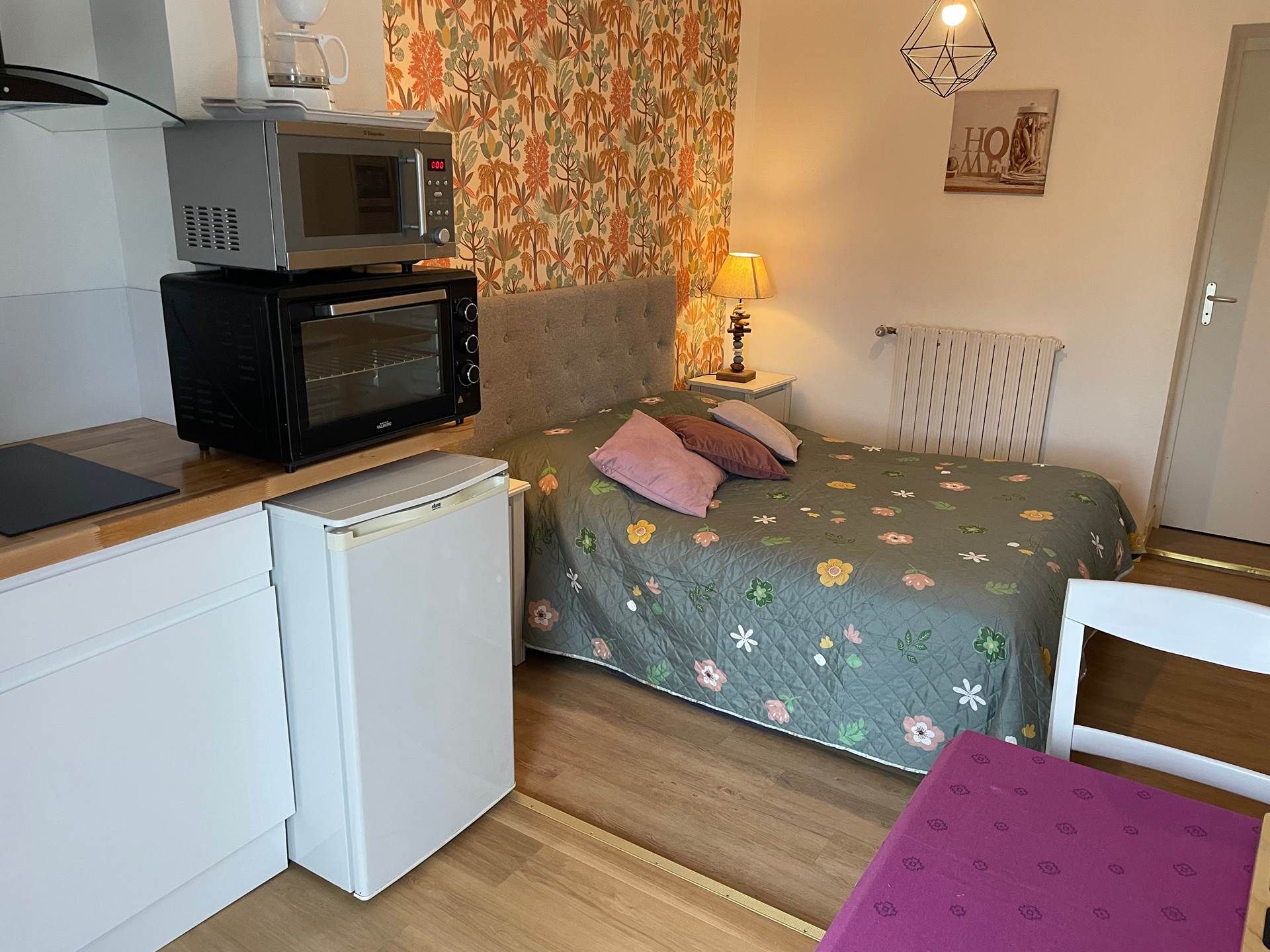 Habitación compacta con cama, microondas, pequeño refrigerador y una mesa con silla.