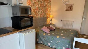 Ein kompaktes Zimmer mit einem Bett, einer Mikrowelle, einem kleinen Kühlschrank und einem Tisch mit einem Stuhl.