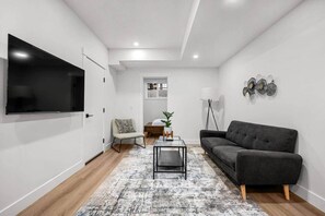 Ein modernes Wohnzimmer mit einem Flachbildfernseher, einem grauen Sofa, einem Couchtisch und einem gemusterten Teppich.