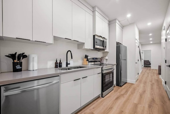 A modern kitchen with white cabinets, stainless steel appliances, and a wooden floor. - The Canopy - Steps to Ctrain and 17th ave (Calgary)