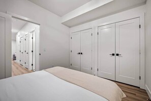 A bedroom with a bed, a wardrobe, and a hallway leading to another room. - The Canopy - Steps to Ctrain and 17th ave (Calgary)