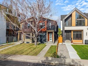 A modern residential building with a well-maintained lawn, a tree in the center, and a clear sky. - The Canopy - Steps to Ctrain and 17th ave (Calgary)