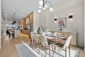 A modern kitchen with wooden cabinets, a dining area with a wooden table and chairs, and a kitchen island with stools. - The Olive - Luxury, 5 min 2 DT, Steps From Ctrain (Calgary)