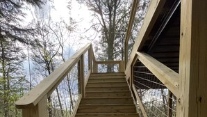 Eine hölzerne Treppe mit Metallgeländern führt zu einer erhöhten Plattform, die von Bäumen umgeben ist.