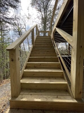 A wooden staircase with metal railings leading to a higher platform surrounded by trees. - Newly Remodeled Mountain Cabin - Hot Tub, Arcade & Fire Pit (Sevierville)