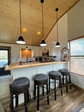 A kitchen with wooden ceiling, white cabinets, a wooden countertop, and three bar stools. - Newly Remodeled Mountain Cabin - Hot Tub, Arcade & Fire Pit (Sevierville)