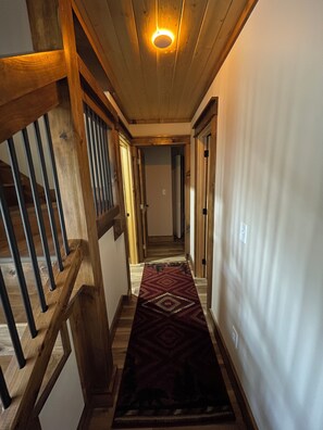 Eine Holztreppe mit Handlauf, einem gemusterten Teppich und einer Leuchte an der Decke.