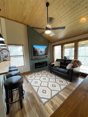 Ein Wohnzimmer mit Fernseher, Kamin, Deckenventilator und einer Bar mit Hockern.