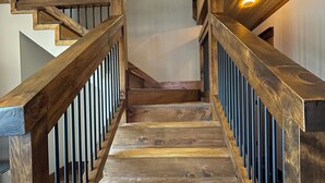 Eine Holztreppe mit Handlauf, die zu einer Zwischenebene mit Deckenleuchte führt.