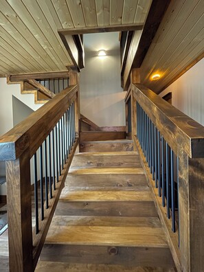 Eine Holztreppe mit Handlauf, die zu einer Zwischenebene mit Deckenleuchte führt.