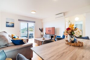 Ein modernes Wohnzimmer mit Sofa, Couchtisch und Fernseher. Es gibt einen Balkon mit Blick.