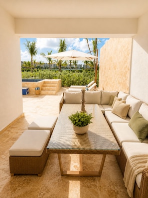 A sunlit outdoor seating area with a pool view, wicker furniture, and a potted plant. - 2BR Crystal Lagoon Retreat Puntacana Prive Pool (Punta Cana)