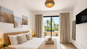 A hotel room with a large bed, a TV, a balcony with curtains, and artwork on the wall. - 2BR Crystal Lagoon Retreat Puntacana Prive Pool (Punta Cana)