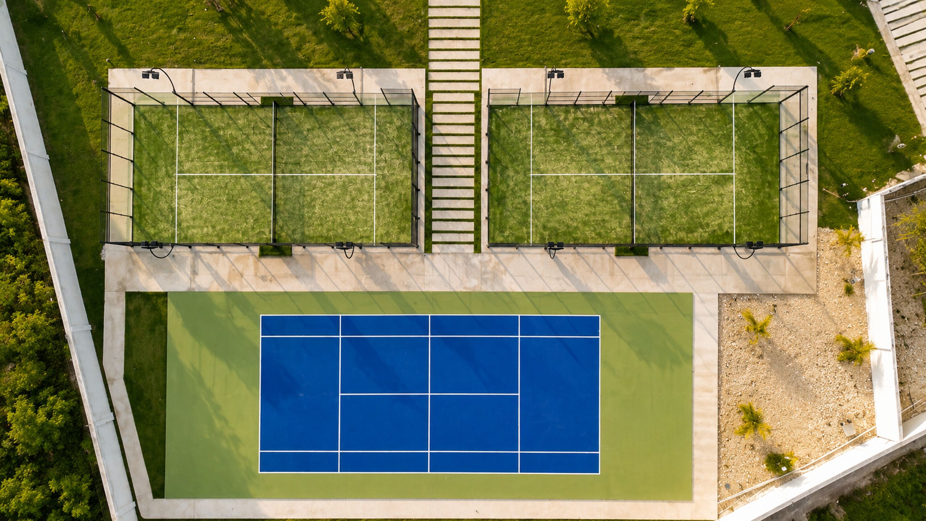 Luftaufnahme eines Tennisplatzes mit zwei angrenzenden Grünflächen, umgeben von einem weißen Zaun.