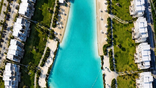 An aerial view of a resort with a large central pool, surrounding buildings, and a beach area. - 2BR Crystal Lagoon Retreat Puntacana Prive Pool (Punta Cana)