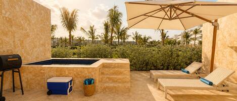 Zona junto a la piscina con un jacuzzi, sillones de descanso y una parrilla.