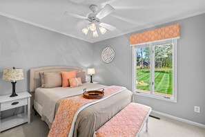 A bedroom with a bed, nightstands, a ceiling fan, a window with a view of a lawn, and a decorative wall clock. - NEW! Hot Tub, Large Dock, Sunset Views | Sleeps 11 (Mooresville)