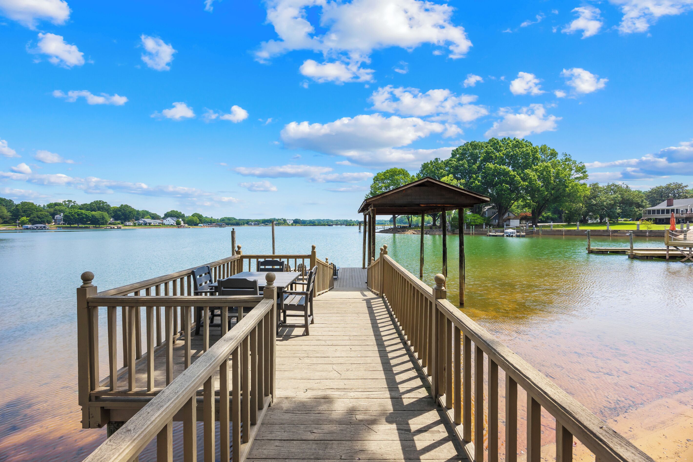 A wooden pier leading to a gazebo with a view of a lake and distant buildings.